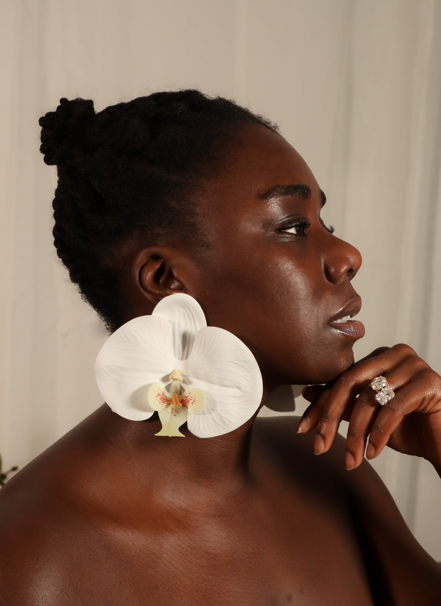 Woman with a white orchid on her shoulder against a neutral background