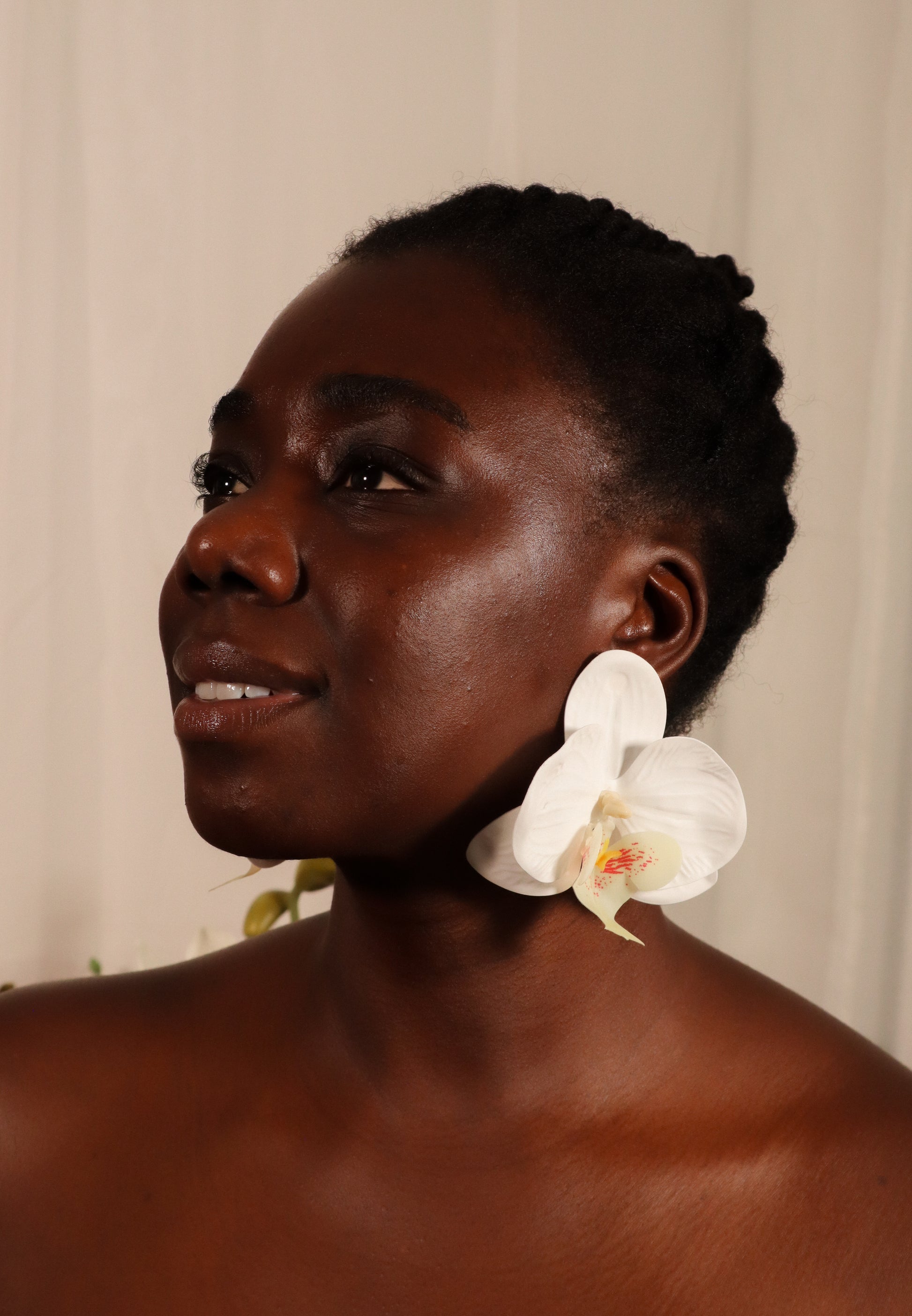 Woman with a white orchid earring against a neutral background
